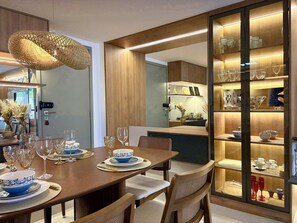 A dining area with a wooden table set for a meal, a glass cabinet with decorative items, and a hanging light fixture. - Falésia Seixas – Charme à Beira-Mar (João Pessoa)