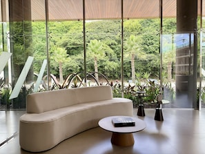A modern interior with a curved sofa, a round table, and a view of lush greenery outside. - Falésia Seixas – Charme à Beira-Mar (João Pessoa)