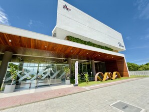 A modern building with a glass entrance, a wooden overhang, and a sign that reads 'Felicidade.' - Falésia Seixas – Charme à Beira-Mar (João Pessoa)