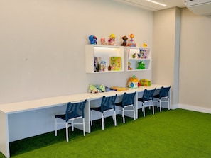A children's play area with a white table, blue chairs, and shelves with toys and books. - Falésia Seixas – Charme à Beira-Mar (João Pessoa)