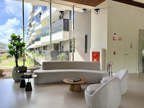 A modern interior with a curved sofa, a round wooden coffee table, and a potted plant. - Falésia Seixas – Charme à Beira-Mar (João Pessoa)