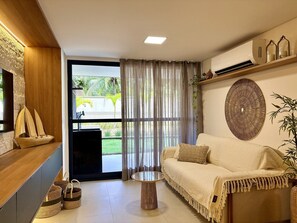A modern living room with a sofa, a small round table, and a decorative wall piece. - Falésia Seixas – Charme à Beira-Mar (João Pessoa)
