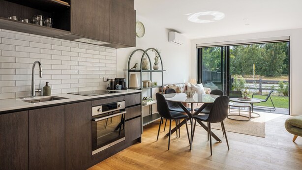 Una cocina moderna con horno integrado, un lavamanos y una zona de comedor con mesa y sillas.
