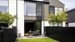 Una casa moderna de dos pisos con un patio, puerta corrediza de vidrio y cerca negra.