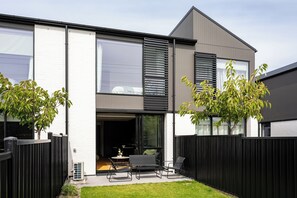 A modern two-story house with a patio, a sliding glass door, and a black fence. - Relaxing Wānaka Townhouse (Wānaka)
