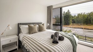 Un dormitorio con cama, mesita de noche, lámpara y vistas a una carretera y árboles.