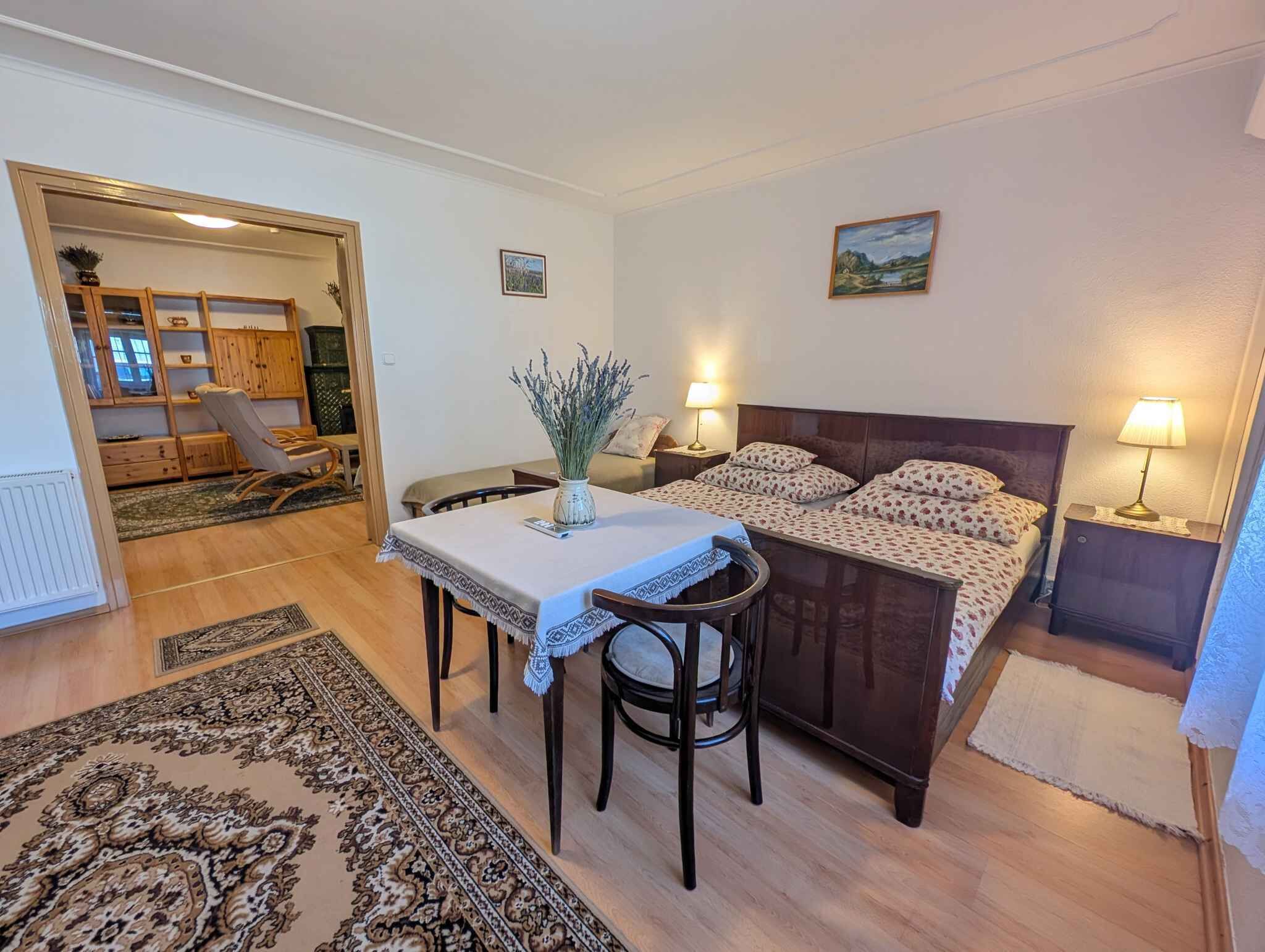 A bedroom with a bed, bedside lamps, a table with a chair, a rug, and a view of a dining area.