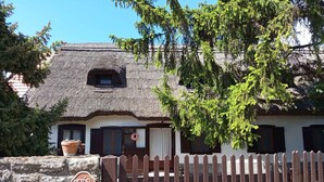 Una casa rústica amb teulada de palla, mur de pedra, porta de fusta i indicació que accepta mascotes.
