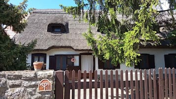Une maison de campagne traditionnelle avec un toit de chaume, un mur en pierre, un portail en bois et une enseigne indiquant qu’elle accepte les animaux de compagnie.
