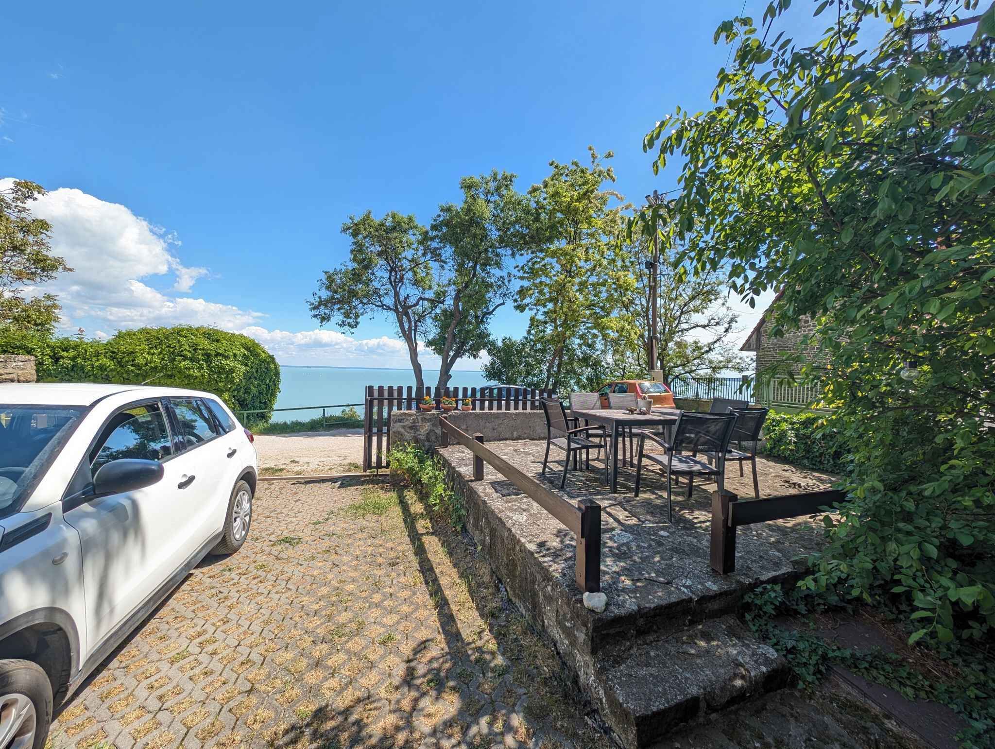 A paved area with a car, outdoor seating, and a view of the sea.