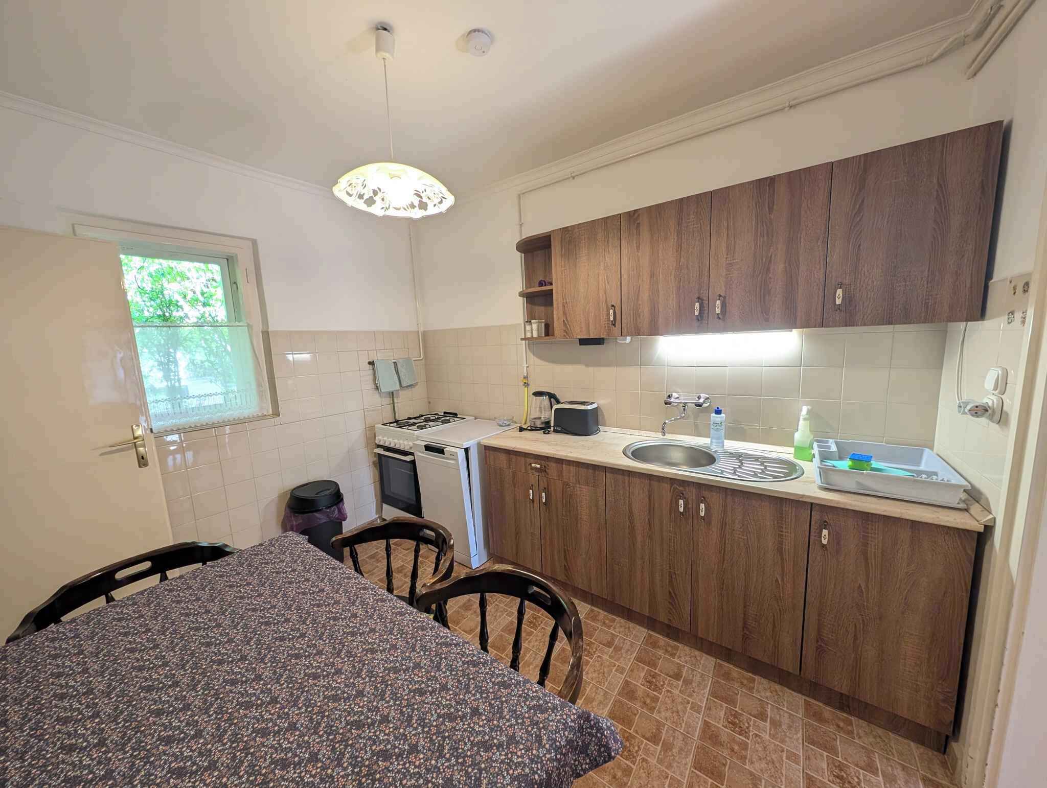 A compact kitchen with a gas stove, sink, wooden cabinets, and a dining table with chairs.