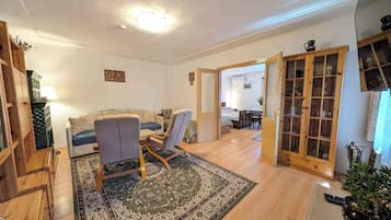 A living room with a sofa, two chairs, a wooden cabinet, and a patterned rug.