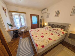 A bedroom with a bed, a desk, a chair, a radiator, and a window.