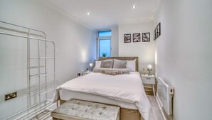Een slaapkamer met een bed, nachtkastjes, een radiator, een raam en wanddecoratie.