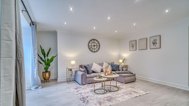 Een moderne woonkamer met een zithoek, een salontafel, een potplant en een wandklok.