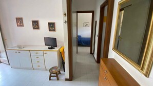 Een kamer met een bureau, computer, stoel, klein krukje, kledingkast en spiegel.