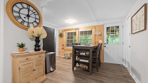 A kitchen with a clock, wooden cabinets, a refrigerator, a dining table with chairs, and a door with windows. - Creekside Chalet near Helen (Cleveland)