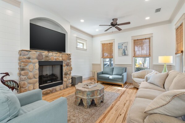 A living room with a stone fireplace, a flat-screen TV, a ceiling fan, and two sofas. - Grayton Beach, Golf cart, Bikes, Heron Cottage, Sleeps 10 (Santa Rosa Beach)