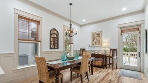 Comedor con mesa de madera, sillas de mimbre, candelabro y ventanas grandes.