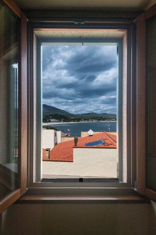 Blick aus einem Fenster auf eine Küstenlandschaft mit Gebäuden und einem Wasserabschnitt.