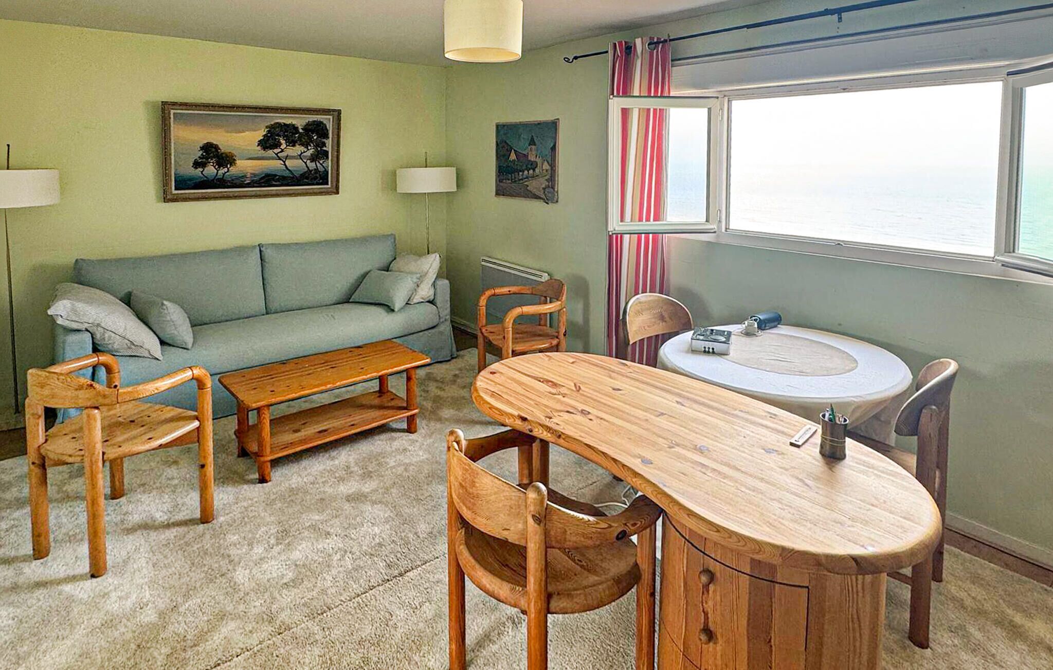 A room with a sofa, two wooden chairs, a wooden table, a window with curtains, and a painting on the wall.