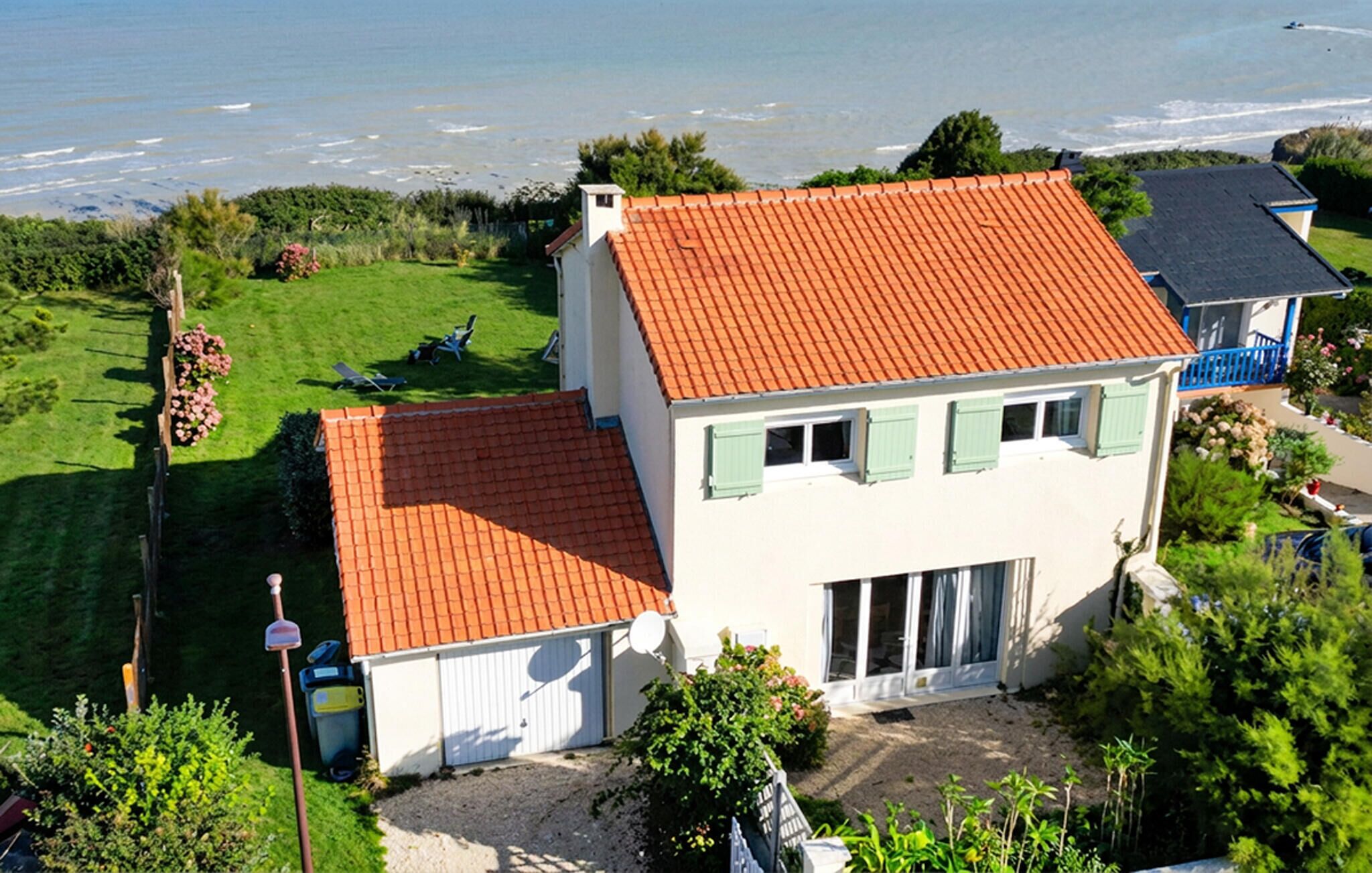 Et tosidet hus med rødt tegltag, garage og græsplads med et par stole.