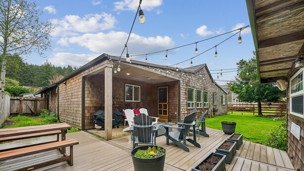 Une terrasse en bois avec des meubles d’extérieur, des guirlandes lumineuses et un espace abrité équipé d’un barbecue.