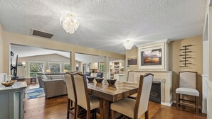Un vaste espace de vie comprenant une table à manger en bois, des sièges confortables, une cheminée et une cuisine à l’arrière-plan.