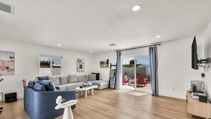 Una sala moderna con sofá, una mesa de centro y un sillón azul. Hay un ventanal corredero que da a un espacio exterior con muebles rojos.