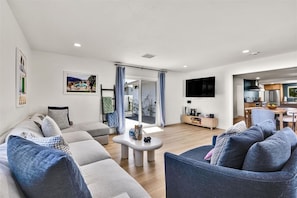 A modern living room with a sofa set, a coffee table, a flat-screen TV, and a sliding glass door leading to a balcony. - Desert Daydream - A Ryson Property (Palm Springs)