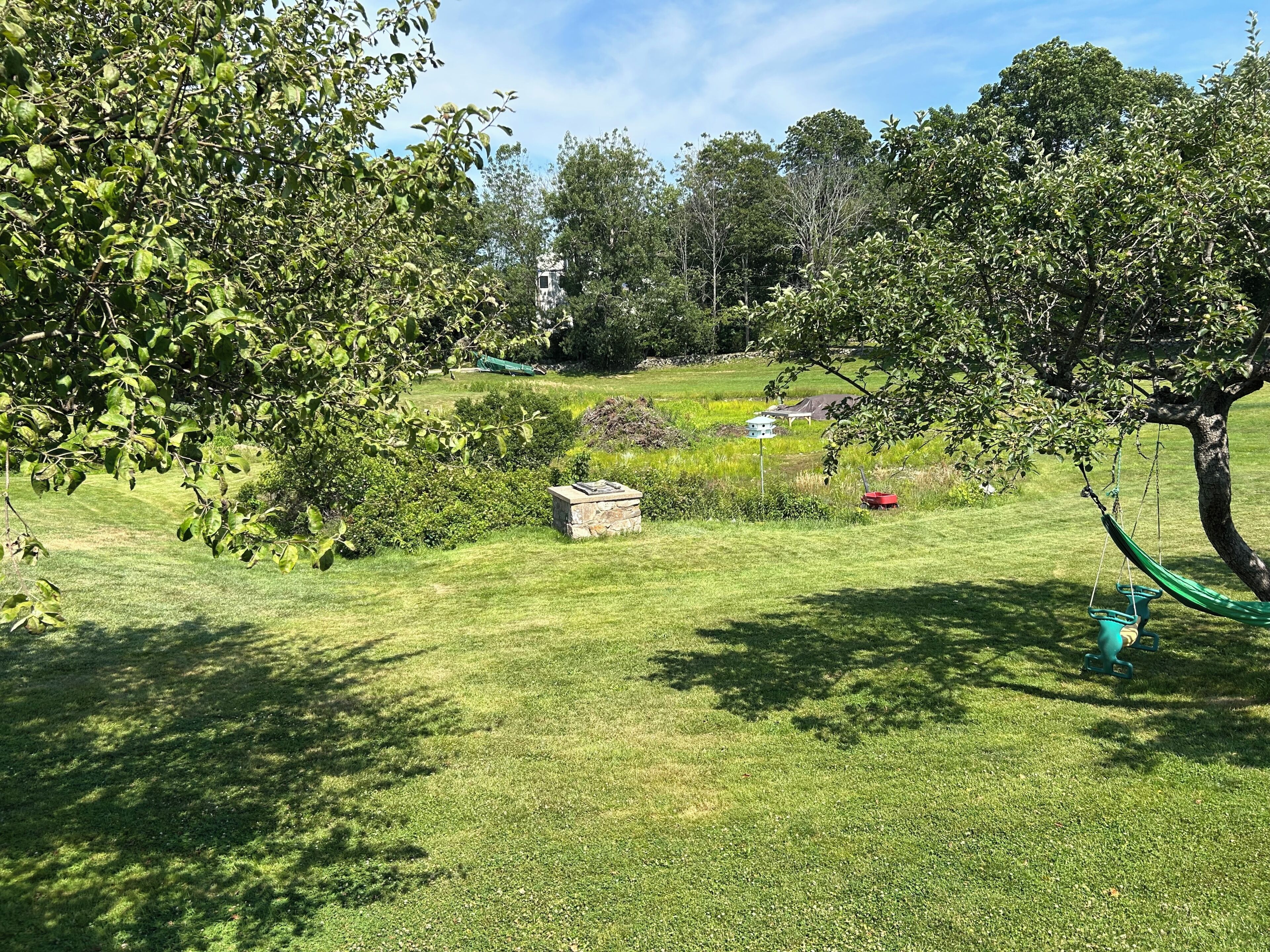 Un'area verde curata con alberi, una struttura in pietra e un'amaca.