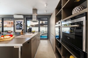 A modern kitchen with a built-in oven, a large island with a cutting board, and a view of the outside.