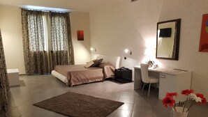 A bedroom with a bed, bedside table, desk, chair, and a small table with flowers. - Hotel Saturday (Palma Campania)