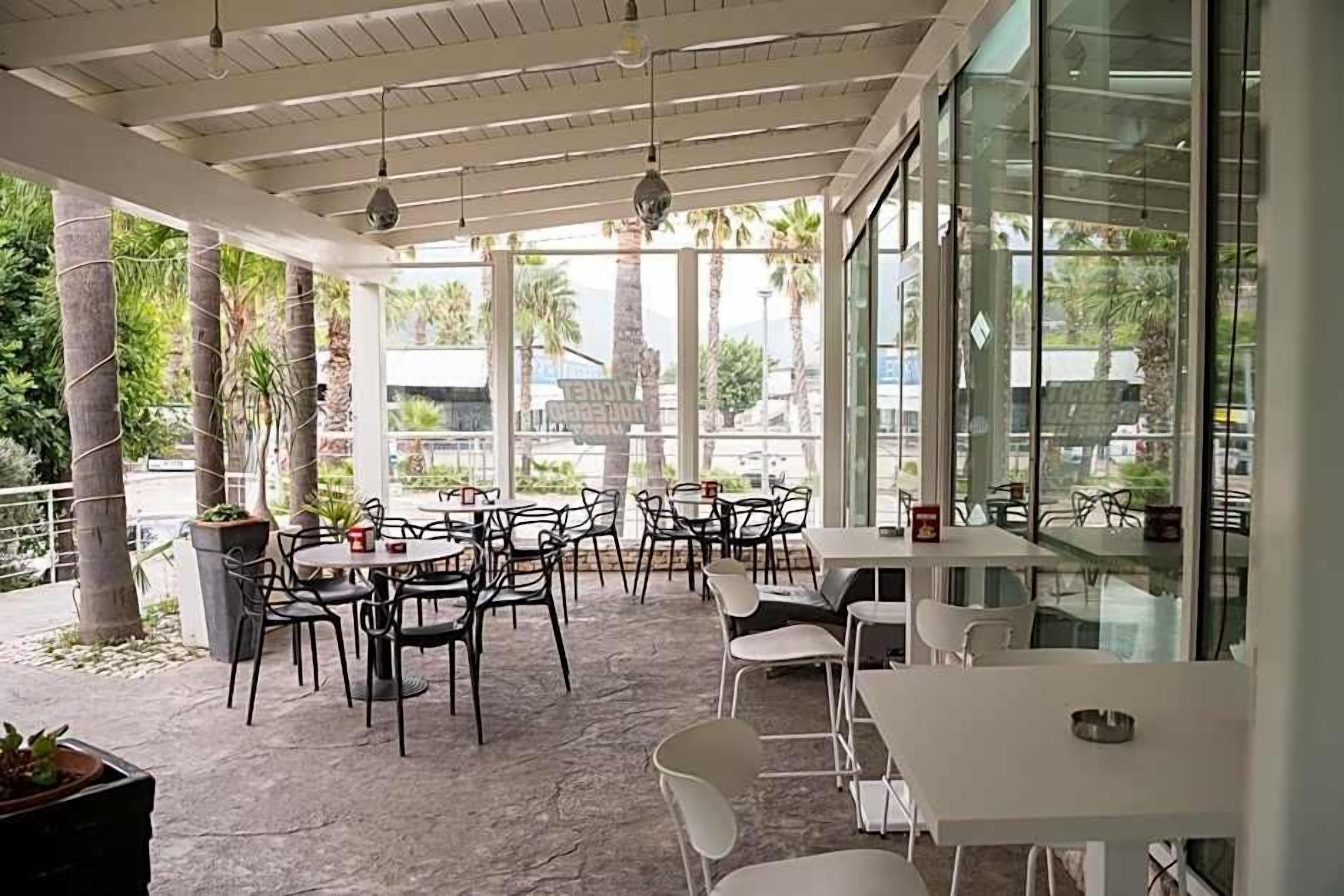 Un caffè all'aperto con tavoli e sedie, ampie finestre e vista su palme.