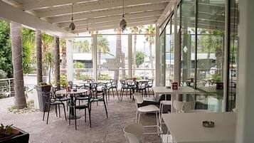 Un caffè all'aperto con tavoli e sedie, ampie finestre e vista su palme.
