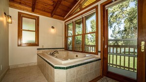 A bathroom with a large bathtub, wooden ceiling, and a door leading to a deck. - Riverside Holiday Home Sleeps 10 (Anderson)