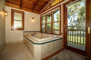 A bathroom with a large bathtub, wooden ceiling, and a view through a door. - Riverside Holiday Home Sleeps 10 (Anderson)