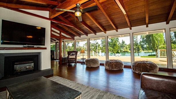 A spacious living area with a fireplace, comfortable seating, a large TV, and large windows offering a view of the outdoors. - Riverside Holiday Home Sleeps 10 (Anderson)