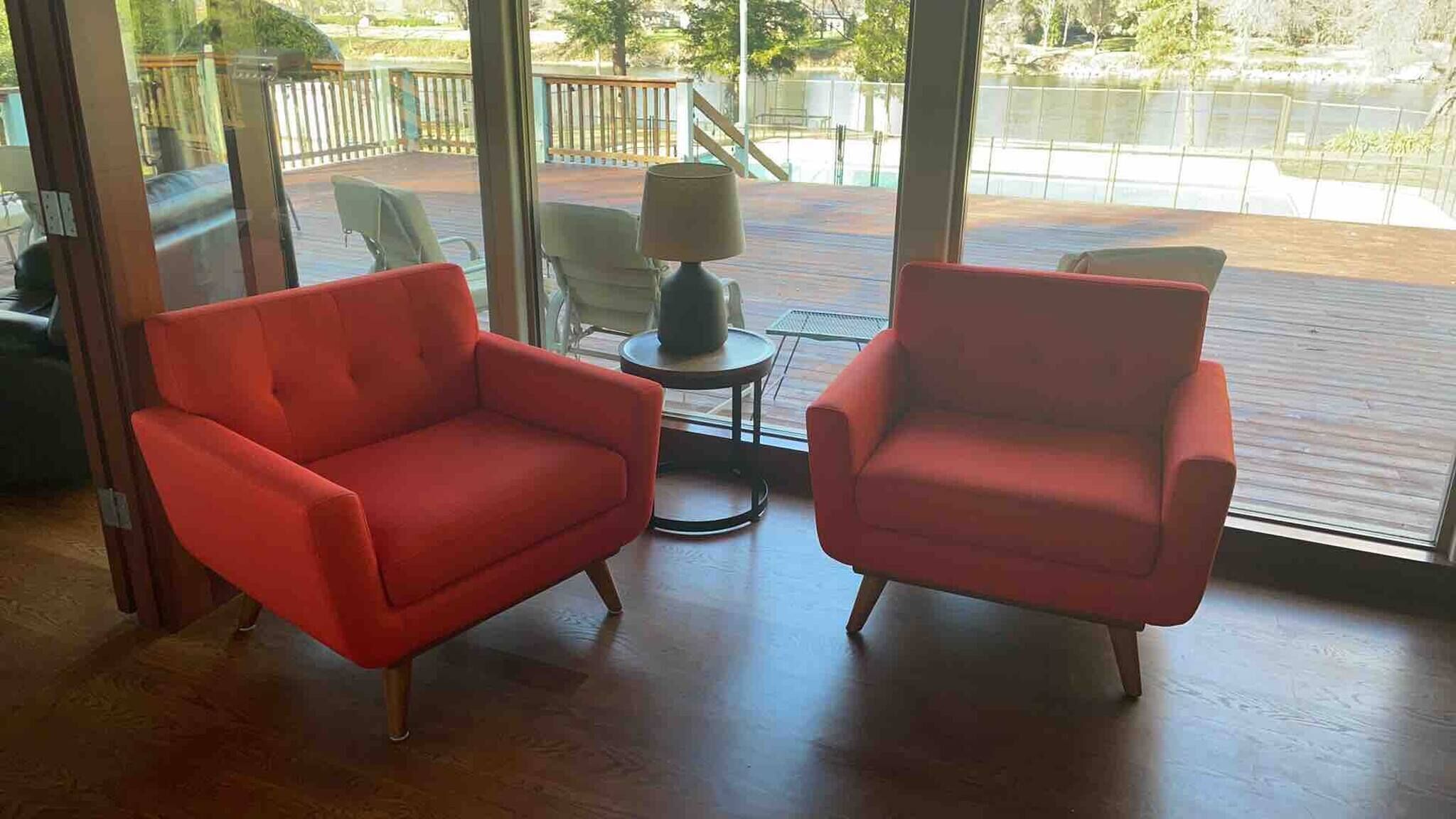 Una habitación con dos sillones rojos, una pequeña mesa con una lámpara y vistas a una piscina a través de amplios ventanales.