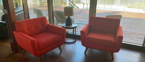 Una habitación con dos sillones rojos, una pequeña mesa con una lámpara y vistas a una piscina a través de amplios ventanales.