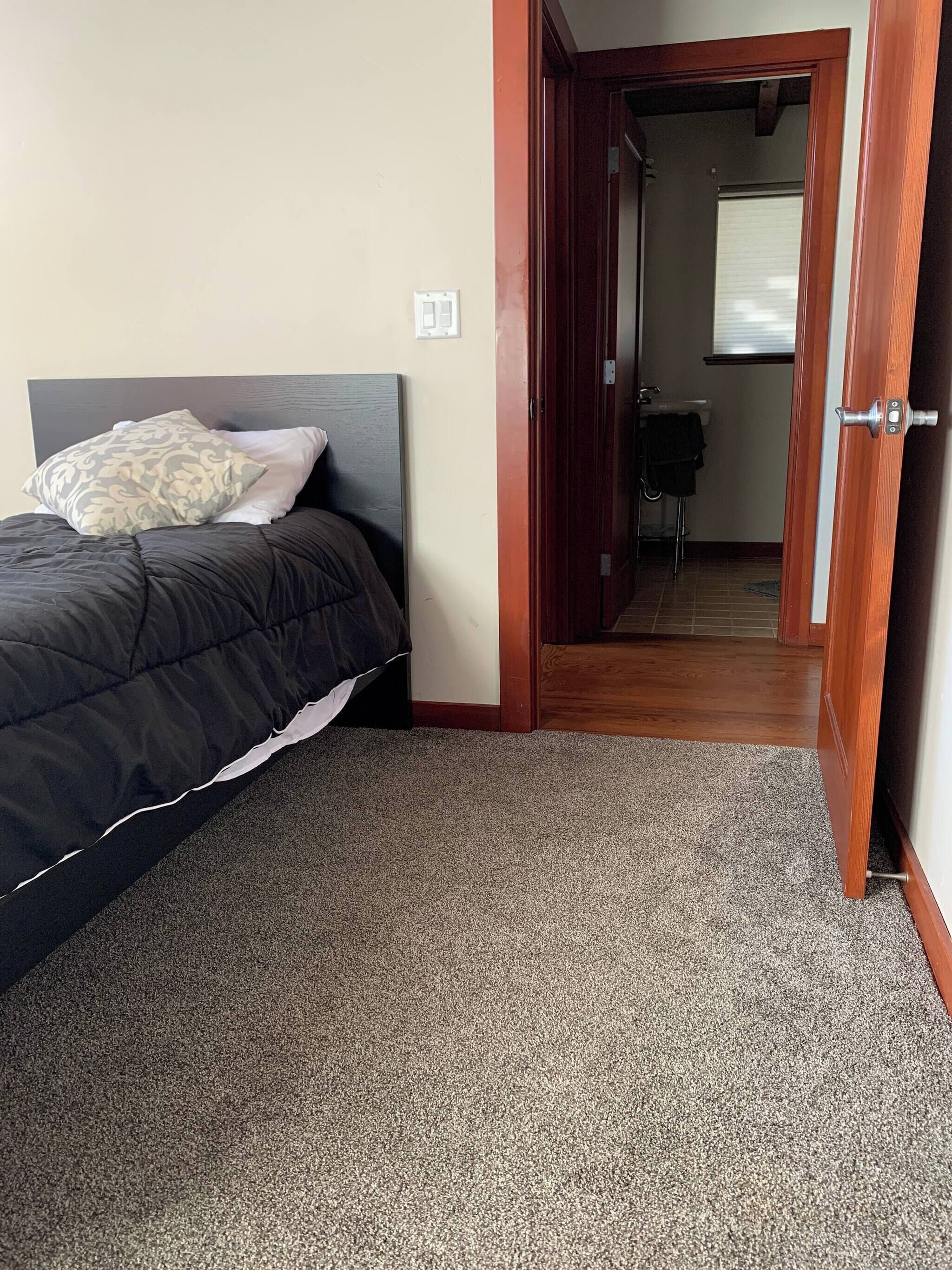 A bedroom with a bed, a door leading to a bathroom, and a carpeted floor.