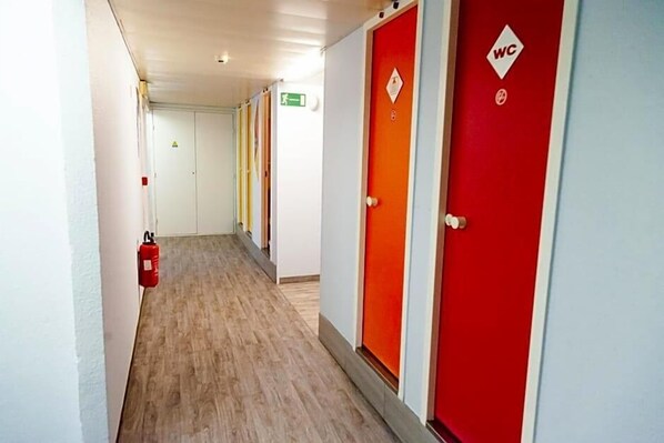 A hallway with a fire extinguisher, a red WC, and a green exit sign. - Formule1 Charleroi (Charleroi)
