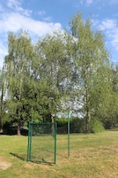Área cercada con una verja verde, rodeada de árboles y césped.