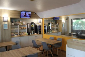A modern dining area with wooden tables and chairs, a kitchen area with appliances, and a television mounted on the wall. - Formule1 Charleroi (Charleroi)