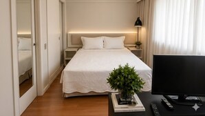 Ein Hotelzimmer mit einem Bett, Nachttischen, einem Fernseher, einer Fernbedienung, einer Pflanze und einem Buch mit dem Titel 'Chanel'.