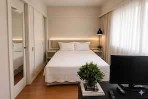 Ein Hotelzimmer mit einem Bett, Nachttischen, einem Fernseher, einer Fernbedienung, einer Pflanze und einem Buch mit dem Titel 'Chanel'.