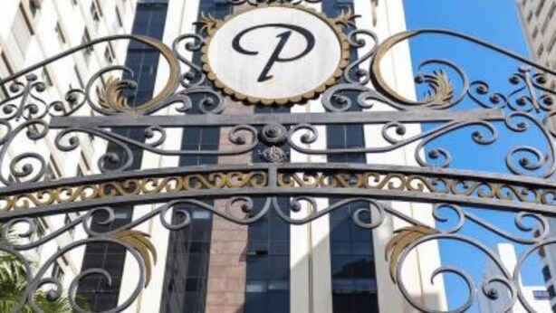 Ein Gebäudeeingang mit auffälligem 'P'-Logo, hohen Glasfenstern und aufwendiger Metallverzierung.
