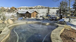 Area termale con una veranda in legno, un paesaggio innevato e un edificio sullo sfondo.
