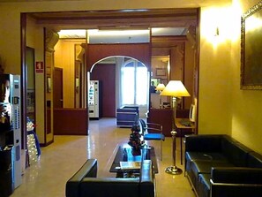 En hotellobby med receptionsdisk, siddeområde og en stor buegang, der fører til et andet rum.