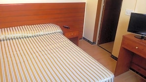 A hotel room with a bed, a wooden headboard, a television on a wooden stand, and a door leading to another room. - Toledano (Barcelona)